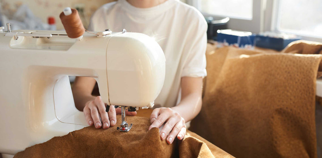Tailor sewing brown leather fabric with a sewing machine in a sunlit workspace